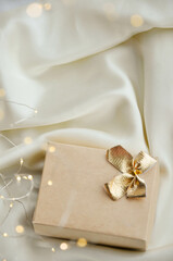 Minimalist Christmas Gift Box on Elegant White Fabric. Aesthetic Christmas composition with a beige gift box tied with a golden bow, resting on a white fabric background. Minimalist design perfect for