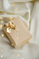 Minimalist Christmas Gift Box on Elegant White Fabric. Aesthetic Christmas composition with a beige gift box tied with a golden bow, resting on a white fabric background. Minimalist design perfect for