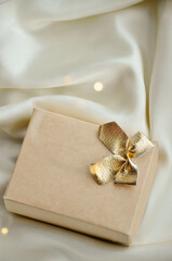 Minimalist Christmas Gift Box on Elegant White Fabric. Aesthetic Christmas composition with a beige gift box tied with a golden bow, resting on a white fabric background. Minimalist design perfect for