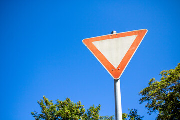 german give way sign with blue sky in the background and trees on the side