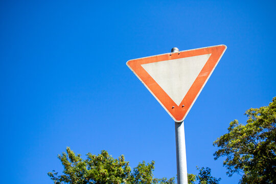 german give way sign with blue sky in the background and trees on the side