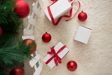 Obraz premium Christmas scene with red baubles and white gift boxes on a fluffy carpet beside a tree