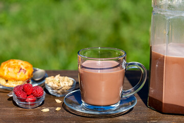 Indian masala chai or tea or cacao in glass with jug and raspberry muffin on the table in cafe on nature background, close up. Trendy healthy drink