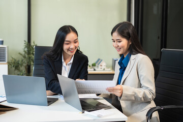 Obraz premium Asian manager mentor talking to young Asian female coworker, showing online project results at meeting. Two happy diverse professional executives team working in office using pc laptop.