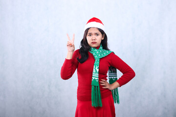 gesture of Asian woman wearing red sweater party wear with Santa hat and scarf, serious face hands sign swear peace, celebrating christmas and new year isolated on white background