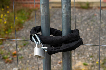 Padlock securing a chain around two metal posts by a fence