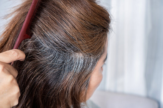 woman with gray hair from back view combing her damaged hair, dry split ends caused by chemicals from hair dye