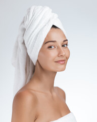 Beautiful young woman with smooth skin and a towel wrapped around her hair, smiling confidently...