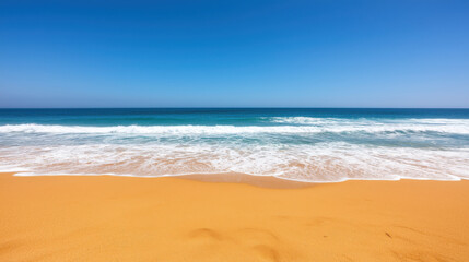 Obraz premium Golden sandy beach with gentle waves under clear blue sky