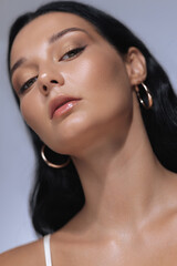 Close-up, low-angle shot of a confident woman with black hair, hoop earrings, and glowing skin,...