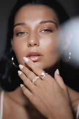 A closeup of a woman with radiant skin and soft makeup, highlighting her elegant hands adorned with...