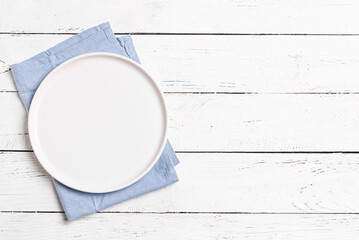 Empty plate and blue napkin on white wooden table