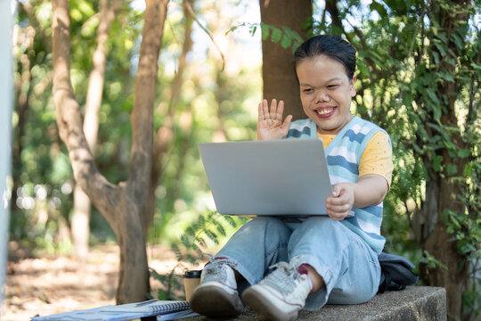 Asian woman with dwarfism video calling in park using laptop outdoors