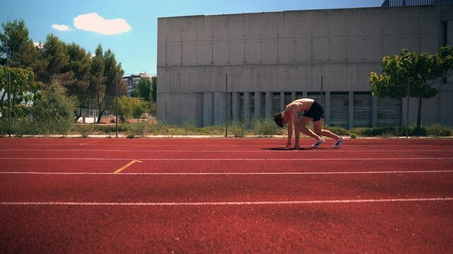 Rear view of a young male athlete running off from his starting position on an athletic track at a stadium. Man sprinting and training outside on a sports ground. Active endurance runner doing cardio