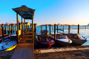 Dock in Venice indicating a water taxi service. Several small boats are moored at the dock, with a...