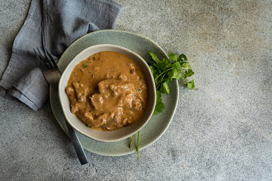 Overhead view of a bowl of beef stroganoff with fresh coriander and a glass of white wine