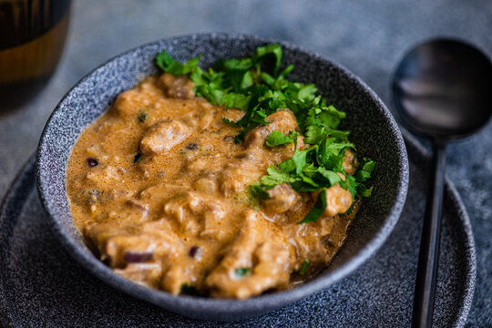 Close-up of a bowl of beef stroganoff with fresh coriander and a glass of white wine
