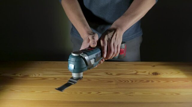 A skilled user demonstrates remarkable precision with an oscillating tool as they work on a sturdy wooden table. Cordless multi cutter in hands
