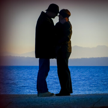 Silhouette of a senior couple standing face to face by the sea with a mountain backdrop, Victoria, British Columbia, Canada