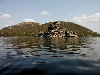 A serene lake surrounded by hills and rocky formations, reflecting the bright blue summer sky. A perfect blend of tranquility and natural beauty.
