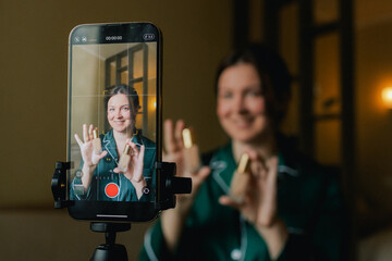 Plus size woman applying makeup on face with brush while recording vlog on smartphone for social...