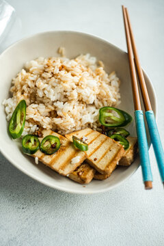Overhead view of a bowl of Rice with slices of barbecued tofu cheese, fresh chillis and soy sauce