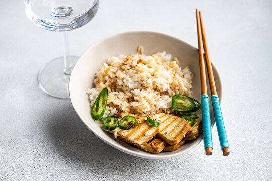 Close-up of a bowl of Rice with slices of barbecued tofu cheese, fresh chillis and soy sauce