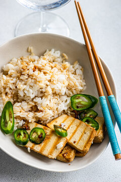 Overhead view of a bowl of Rice with slices of barbecued tofu cheese, fresh chillis and soy sauce