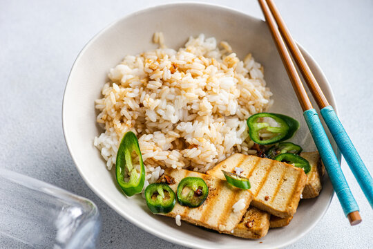 Overhead view of a bowl of Rice with slices of barbecued tofu cheese, fresh chillis and soy sauce
