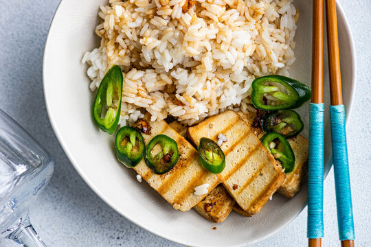 Overhead view of a bowl of Rice with slices of barbecued tofu cheese, fresh chillis and soy sauce