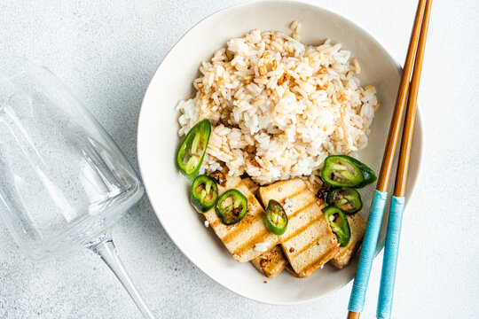 Overhead view of a bowl of Rice with slices of barbecued tofu cheese, fresh chillis and soy sauce
