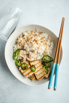 Overhead view of a bowl of Rice with slices of barbecued tofu cheese, fresh chillis and soy sauce