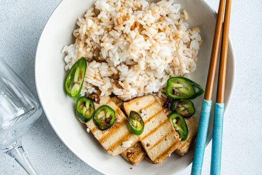 Overhead view of a bowl of Rice with slices of barbecued tofu cheese, fresh chillis and soy sauce