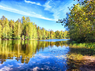 Serene lake surrounded by vibrant autumn trees under a clear blue sky in early afternoon light