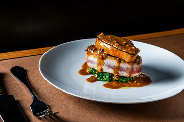 A gourmet dish featuring a thick cut of meat topped with a smaller piece, both covered in a rich...