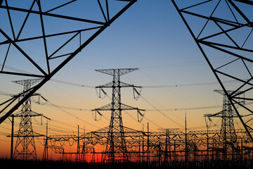 Many high-voltage power towers, silhouetted against the setting sun