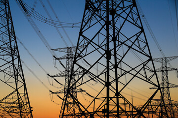 Many high-voltage power towers, silhouetted against the setting sun