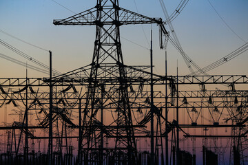 Many high-voltage power towers, silhouetted against the setting sun