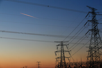Many high-voltage power towers, silhouetted against the setting sun