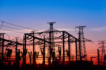 Many high-voltage power towers, silhouetted against the setting sun