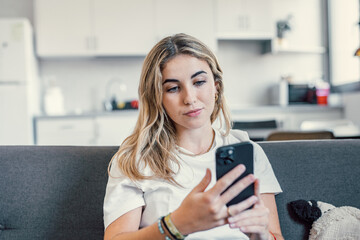 Young beautiful woman sit on sofa in living room using modern smartphone, make call or order at home. Client of e-commerce services, mobile application usage. Technology, connection, lifestyle concept