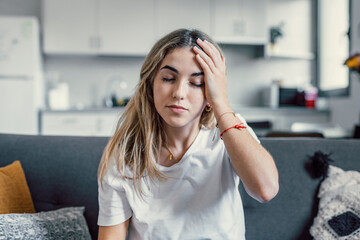 Fototapeta premium Depressed or tired teen girl feeling stress headache hurt pain sitting alone at home, upset sad heartbroken young woman regret pregnancy or abortion, troubled with problem or psychological trauma
