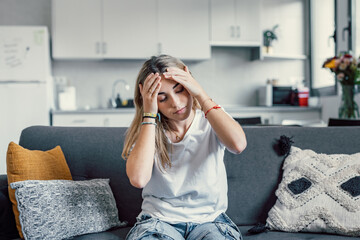 Depressed or tired teen girl feeling stress headache hurt pain sitting alone at home, upset sad...
