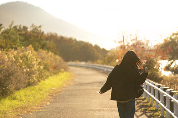 夕方の秋の景色の道を楽しそうに歩く女性の後ろ姿