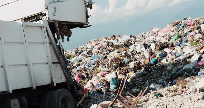 A garbage truck dumping waste at a large landfill under a clear sky