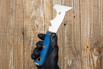 A hand firmly grasping a unique and finely crafted blade tool set against a rustic wooden backdrop