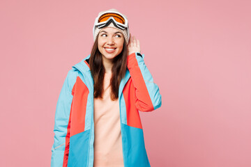 Skier young woman wear warm blue padded jacket ski goggles mask spend extreme weekend winter season in mountains try hear you overhear listen intently isolated on plain pink background. Hobby concept.