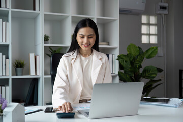 Confident Businesswoman Working on Laptop in Modern Office with Plants and Bookshelves