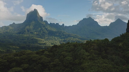Fototapeta premium Scenic aerial perspective of green rainforest blanketing the rugged volcanic mountains peaks, stunning panorama of Moorea tropical island in French Polynesia. Remote wild nature travel background