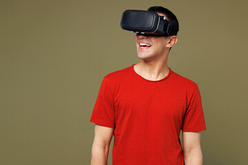 Young smiling happy cheerful cool middle eastern man he wear red t-shirt casual clothes watching in vr headset pc gadget isolated on plain pastel green background studio portrait. Lifestyle concept.